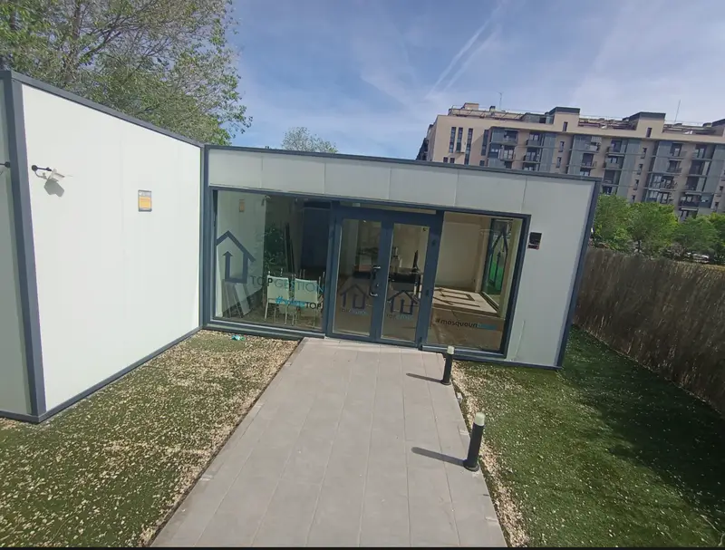 Oficina de ventas modular con fachada acristalada y jardín
